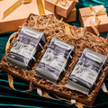 Three bags of Mr. Espresso oakwood-roasted coffee arranged in a gift box with shredded paper, surrounded by ribbon-wrapped packages on dark green velvet.