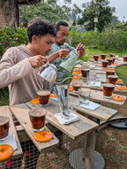 Two men pouring drinks at an outdoor table with a garden background