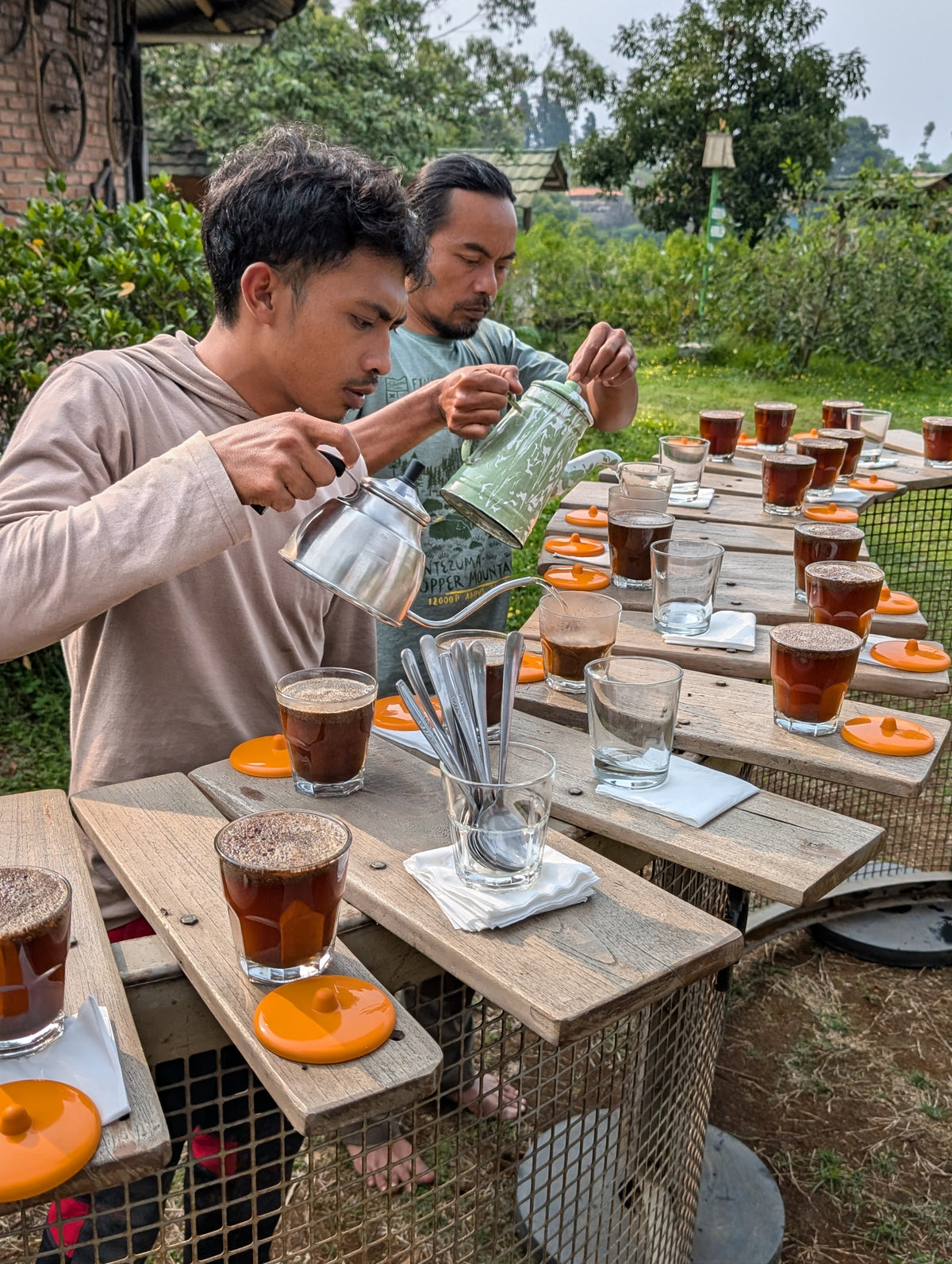 Two men pouring drinks at an outdoor table with a garden background