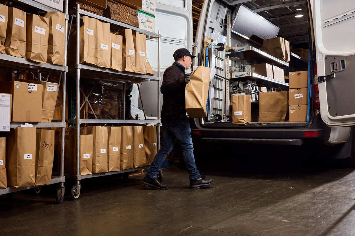 Warehouse staff loading paper bags into a Mr. Espresso delivery van